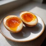 Two halves of a perfectly cooked Shoyu Ramen Eggs Overnight showing jammy, bright orange yolks on a small plate.