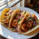 Three delicious Shrimp Baja Tacos with seasoned shrimp and crunchy red and green slaw served on a white plate.