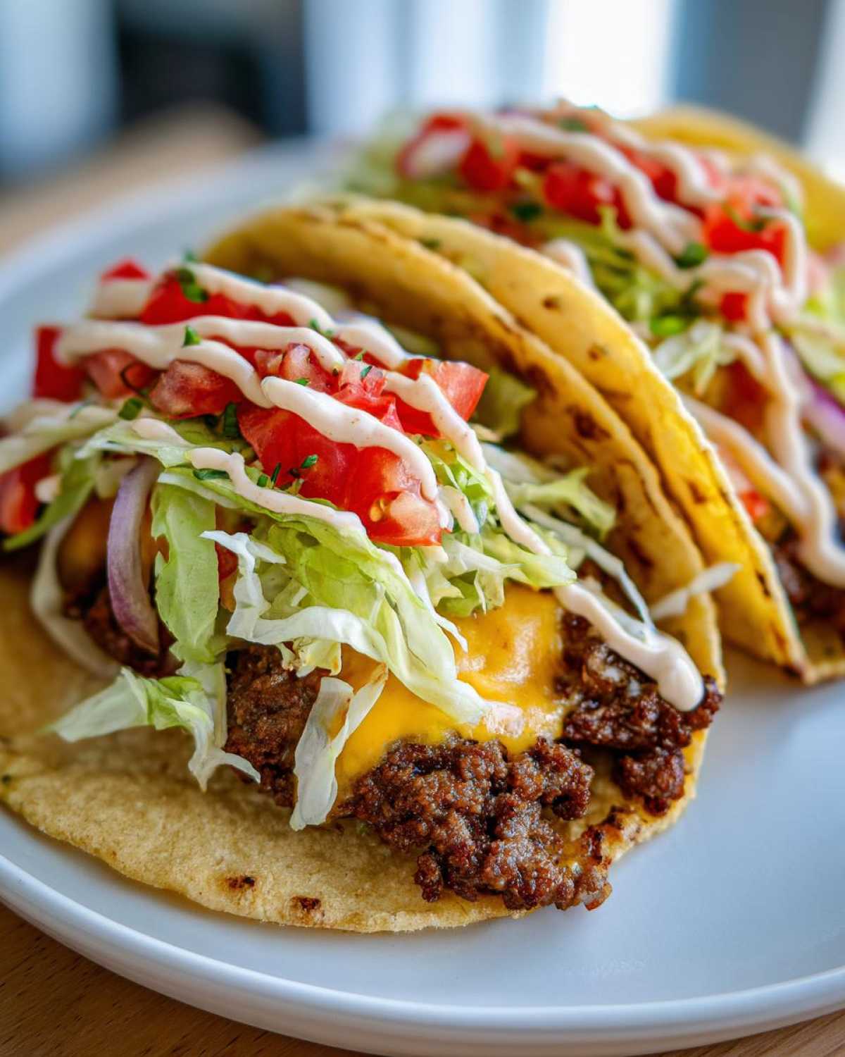 Close-up of two fully loaded Smash Burger Tacos featuring seasoned ground beef, melted cheese, lettuce, tomato, and a white sauce drizzle.