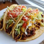 Three fully loaded Smash Burger Tacos featuring seasoned ground beef, shredded lettuce, cheese, diced tomatoes, and a drizzle of white sauce.