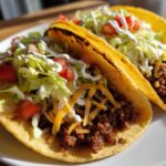 Two crispy tacos filled with seasoned ground beef, shredded cheese, lettuce, tomato, and sour cream, representing delicious Smash Burger Tacos.
