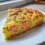 A thick slice of Smoked Salmon Dill Frittata showing chunks of pink salmon and green dill in a fluffy egg base.