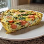 A close-up of a thick slice of Smoked Salmon Dill Frittata, showing pink salmon pieces and green dill baked into the yellow egg base.