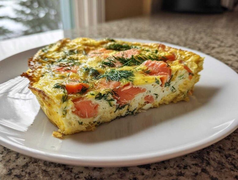 A close-up of a thick slice of Smoked Salmon Dill Frittata, showing pink salmon pieces and green dill baked into the yellow egg base.