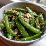 Close-up of a bright green Snap Pea Sesame Salad tossed with sesame seeds and sliced almonds in a white bowl.