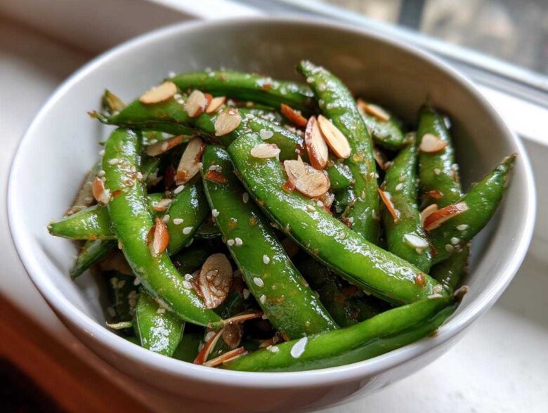 Close-up of a bright green Snap Pea Sesame Salad tossed with sesame seeds and sliced almonds in a white bowl.
