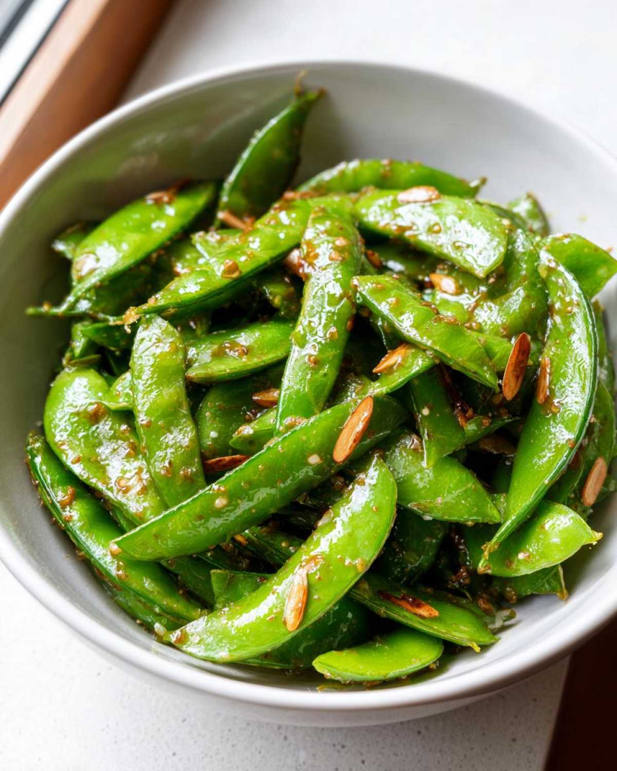 Close-up of a bowl filled with bright green Snap Pea Sesame Salad coated in a savory dressing and sesame seeds.
