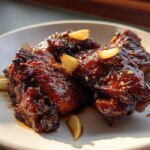 Close-up of glistening, dark Soy Sauce Chicken with Ginger, topped with sliced garlic cloves.