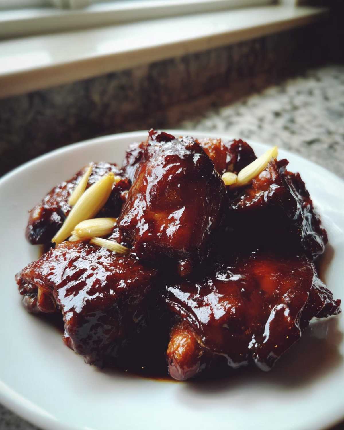 Close-up of glossy, dark Soy Sauce Chicken with Ginger pieces served on a white plate.