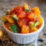 Close-up of diced mango and cucumber pieces generously coated in red chili powder, ready for Spicy Mango Tajin Fruit Cups.