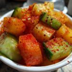 Close-up of diced mango and cucumber pieces heavily coated in red Tajin seasoning in a white cup for Spicy Mango Tajin Fruit Cups.