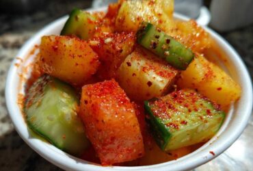 Close-up of diced mango and cucumber pieces heavily coated in red Tajin seasoning in a white cup for Spicy Mango Tajin Fruit Cups.