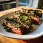 Close-up of perfectly cooked, medium-rare steak sliced and generously topped with vibrant green Carrot Top Chimichurri.