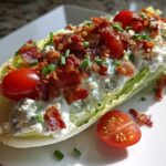 A perfectly dressed Steakhouse Wedge Salad with blue cheese, crispy bacon, and cherry tomatoes on a white plate.