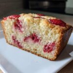 A close-up of a moist slice of Strawberry Almond Flour Snack Cake, studded with bright red strawberries, served on a white rectangular plate.