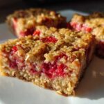 A close-up of a freshly baked Strawberry Baked Oatmeal Breakfast Squares square showing a thick layer of bright red fruit filling.