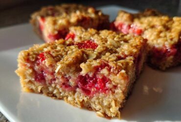 A close-up of a freshly baked Strawberry Baked Oatmeal Breakfast Squares square showing a thick layer of bright red fruit filling.