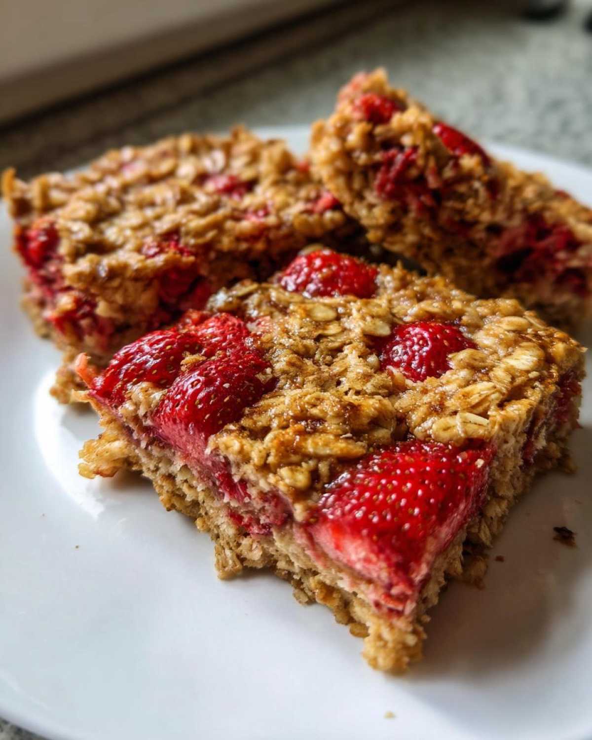Three slices of moist Strawberry Baked Oatmeal Breakfast Squares stacked slightly on a white plate.