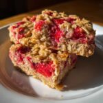 Two stacked squares of moist Strawberry Baked Oatmeal Breakfast Squares showing oats and bright red strawberry filling.