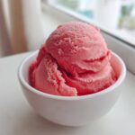 Two scoops of bright pink Strawberry Banana Nice Cream served in a small white bowl.