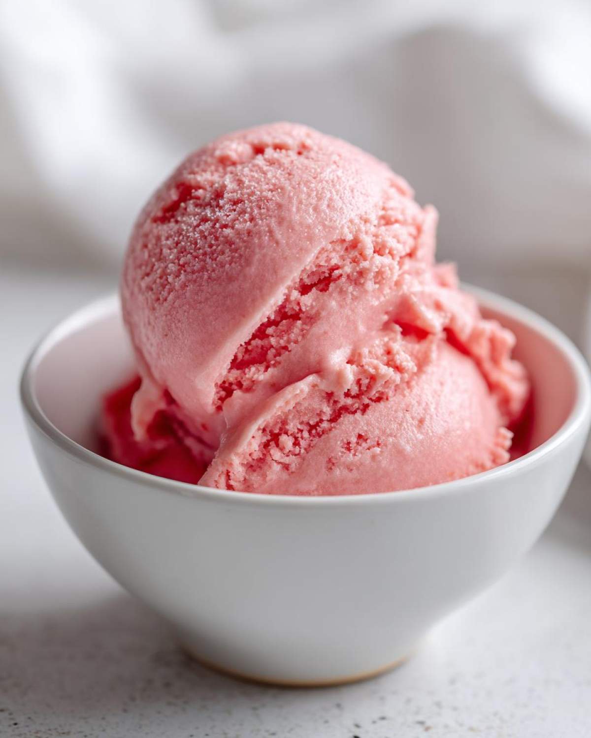 Close-up of two scoops of bright pink Strawberry Banana Nice Cream served in a small white bowl.