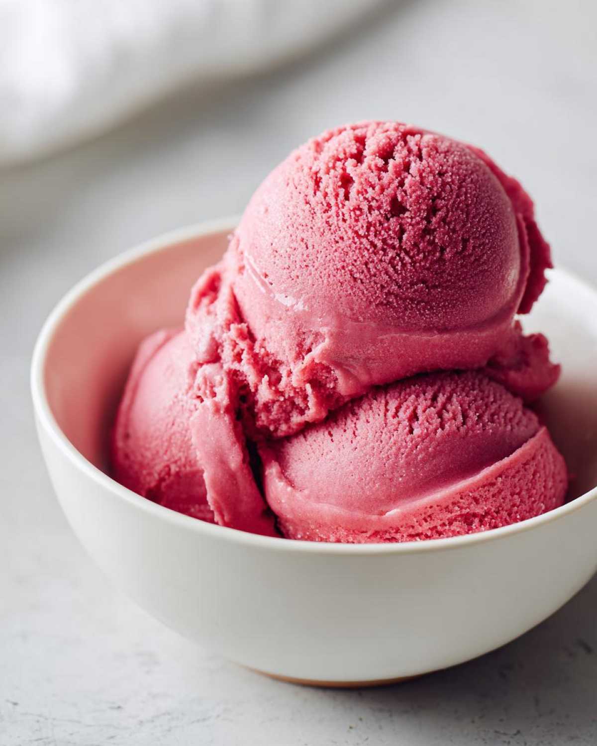 Three scoops of vibrant pink Strawberry Banana Nice Cream served in a small white bowl.