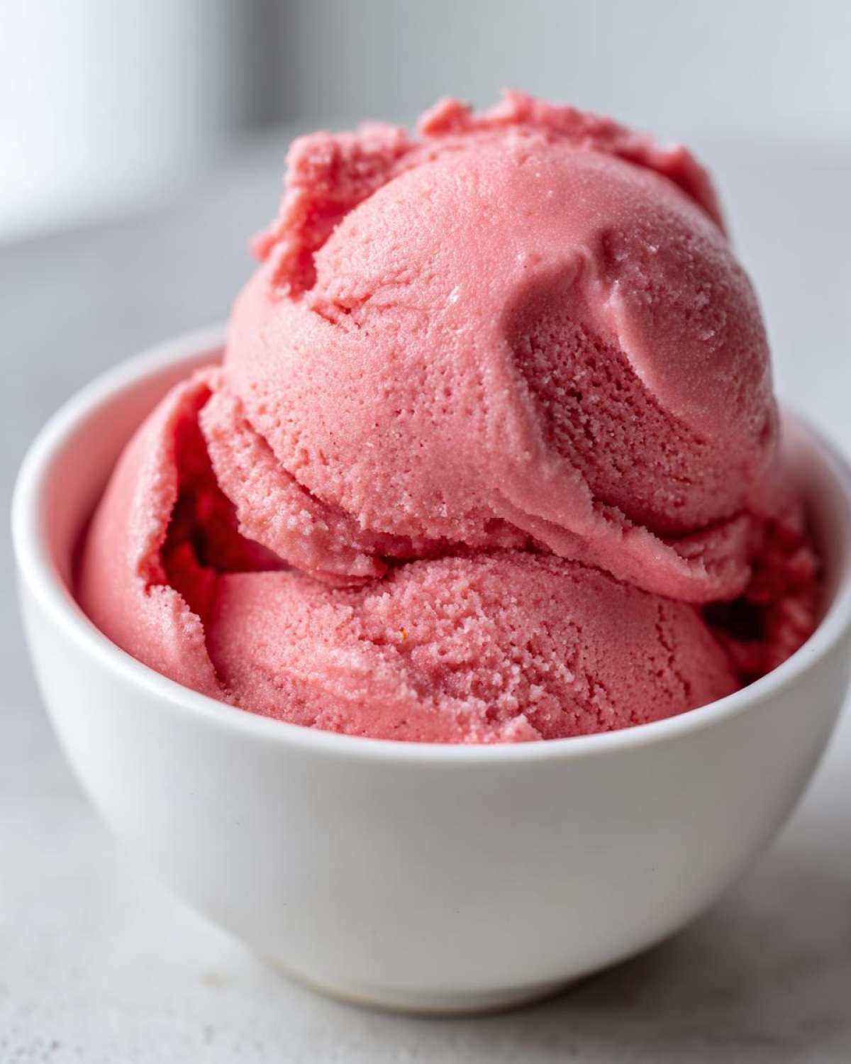 Close-up of freshly blended, bright pink Strawberry Banana Nice Cream scooped into a small white bowl.