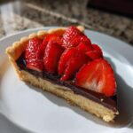 A close-up slice of Strawberry Chocolate Ganache Tart featuring a buttery crust, dark chocolate filling, and glossy sliced strawberries.