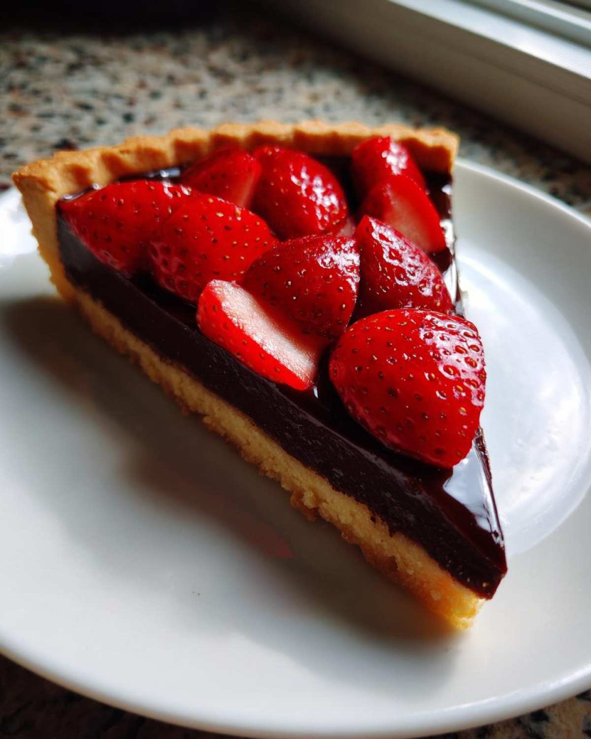 A perfect slice of Strawberry Chocolate Ganache Tart featuring a golden crust, rich dark ganache, and glossy fresh strawberries.