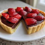 A whole Strawberry Chocolate Ganache Tart with one slice cut out, sitting on a white plate.