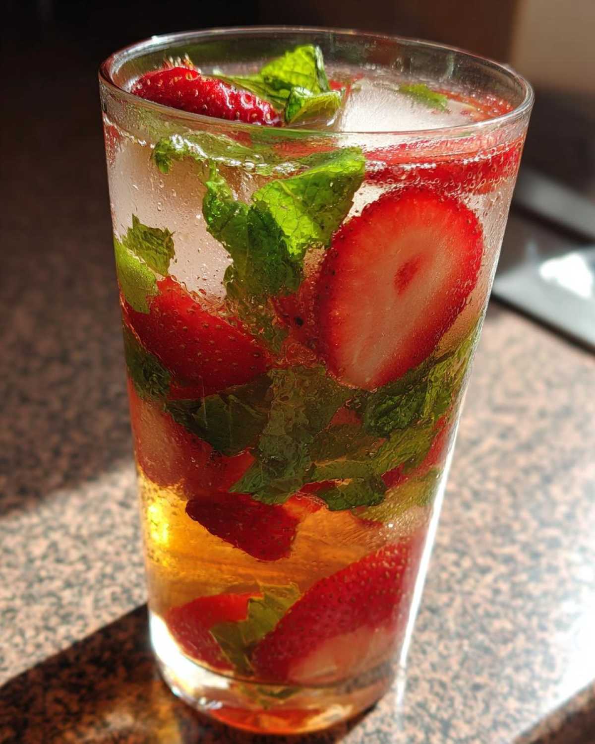 Close-up of a tall glass filled with Strawberry Iced Green Tea with Mint, ice, and fresh strawberry slices.