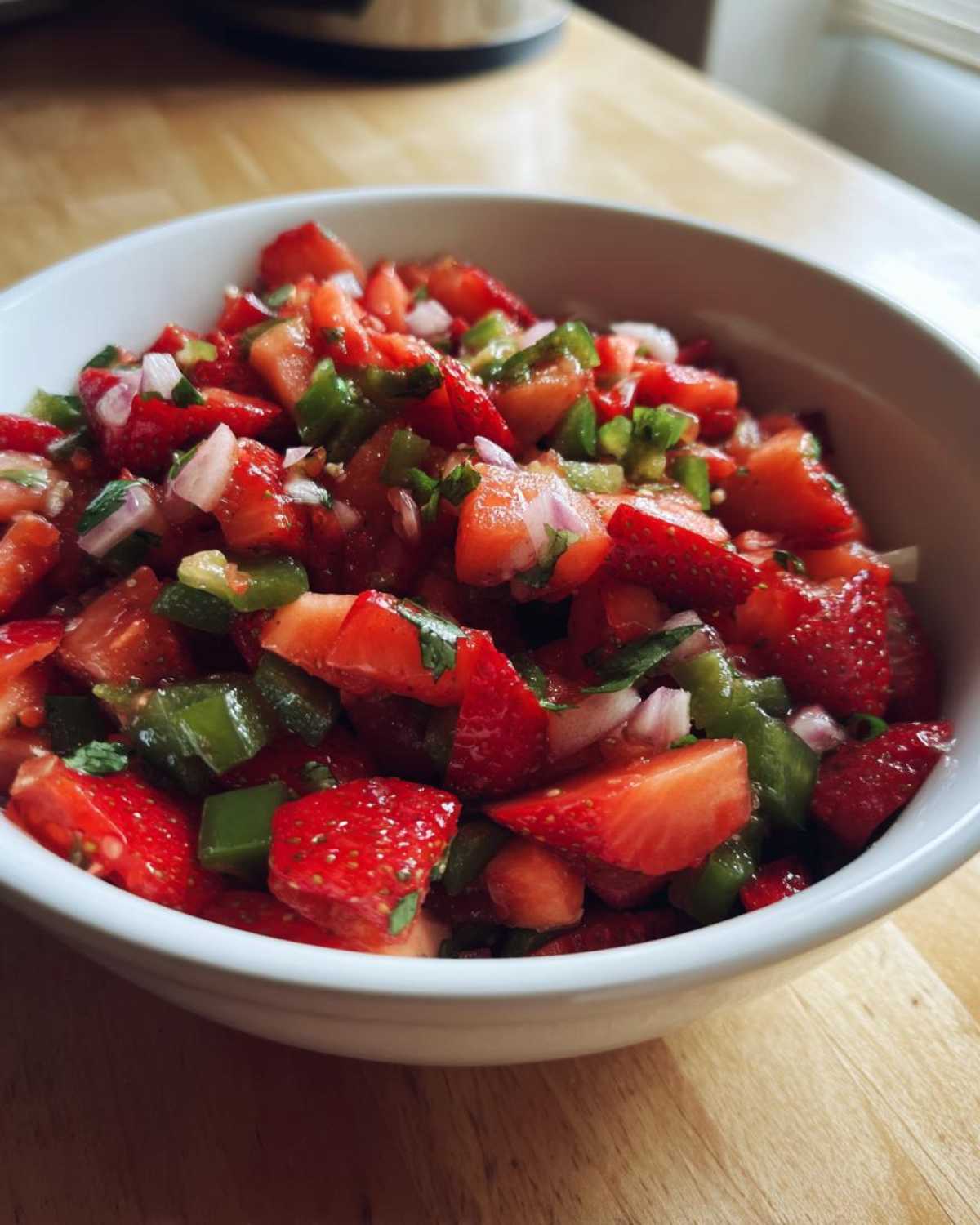 Close-up of vibrant Strawberry Jalapeno Salsa featuring diced strawberries, green peppers, and red onion in a white bowl.