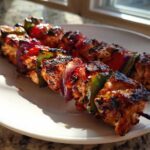 Two skewers of grilled Tequila Lime Chicken Skewers with charred chicken, red onion, and bell peppers on a white plate.