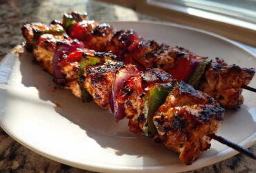 Two skewers of grilled Tequila Lime Chicken Skewers with charred chicken, red onion, and bell peppers on a white plate.