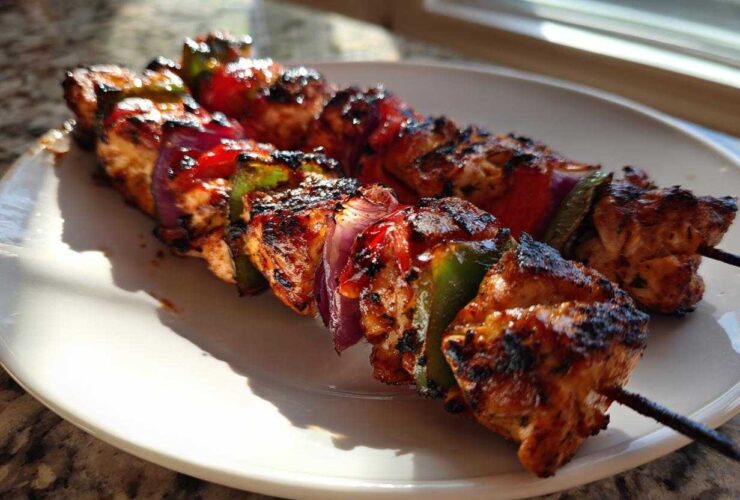 Two skewers of grilled Tequila Lime Chicken Skewers with charred chicken, red onion, and bell peppers on a white plate.