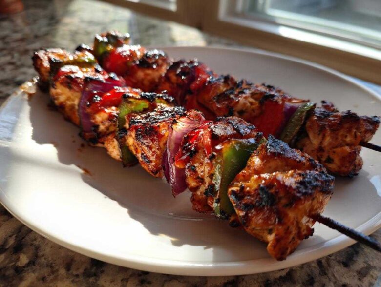 Two skewers of grilled Tequila Lime Chicken Skewers with charred chicken, red onion, and bell peppers on a white plate.