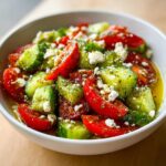 Close-up of a bowl filled with vibrant Tomato Cucumber Feta Salad, dressed in oil and herbs.