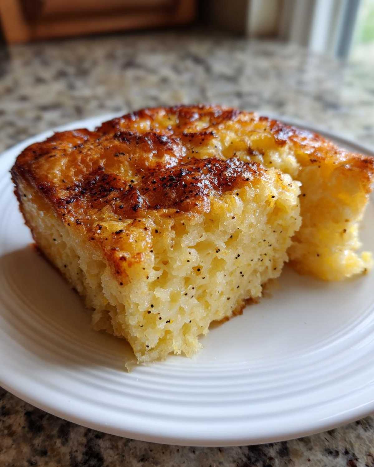 Close-up of a golden-brown slice of Vanilla Bean French Toast Casserole on a white plate.