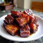 A close-up of rich, sticky Vietnamese Caramel Pork pieces piled high on a white plate, glistening with dark caramel sauce.