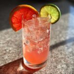 Close-up of a fizzy Virgin Paloma Grapefruit Spritz garnished with grapefruit and lime slices.